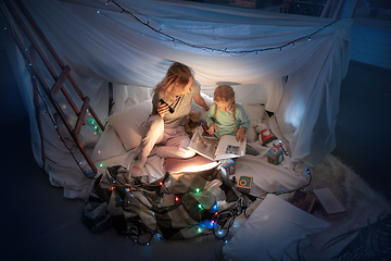 Image showing Mother and daughter sitting in a teepee, reading stories with the flashlight