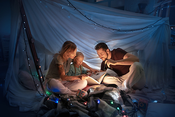 Image showing Family sitting in a teepee, reading stories with the flashlight