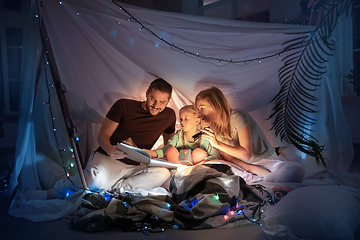 Image showing Family sitting in a teepee, reading stories with the flashlight