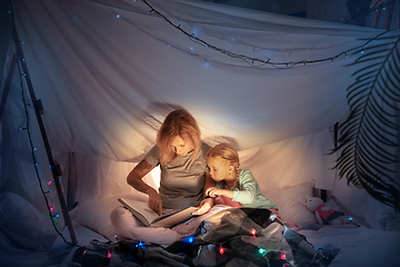 Image showing Mother and daughter sitting in a teepee, reading stories with the flashlight