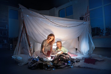 Image showing Mother and daughter sitting in a teepee, reading stories with the flashlight