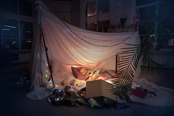 Image showing Little girl lying in a teepee, playing with the flashlight