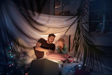 Image showing Father and daughter sitting in a teepee, having fun with the flashlight