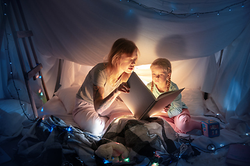 Image showing Mother and daughter sitting in a teepee, reading stories with the flashlight