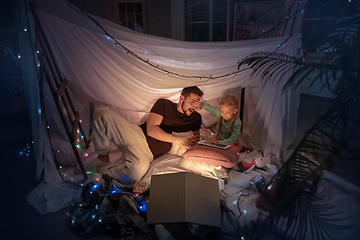 Image showing Father and daughter sitting in a teepee, having fun with the flashlight