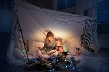 Image showing Mother and daughter sitting in a teepee, reading stories with the flashlight