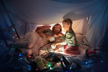 Image showing Mother and daughter sitting in a teepee, having fun with the flashlight