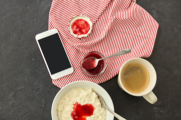 Image showing porridge with jam, spoon, coffee and phone