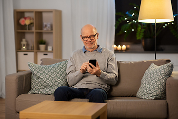 Image showing happy senior man texting on smartphone at home