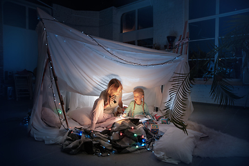 Image showing Mother and daughter sitting in a teepee, reading stories with the flashlight