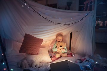 Image showing Little girl lying in a teepee, playing with the flashlight