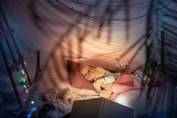 Image showing Little girl lying in a teepee, playing with the flashlight