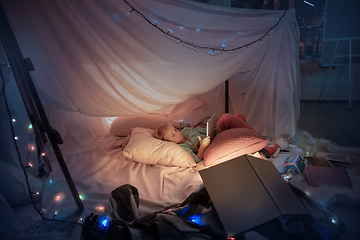 Image showing Little girl lying in a teepee, playing with the flashlight