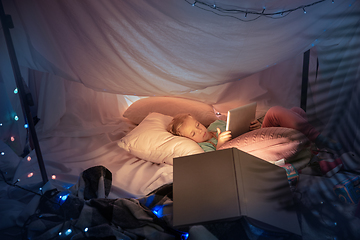 Image showing Little girl lying in a teepee, playing with the flashlight