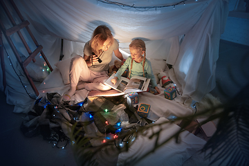 Image showing Mother and daughter sitting in a teepee, reading stories with the flashlight