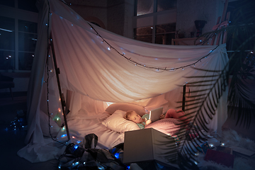 Image showing Little girl lying in a teepee, playing with the flashlight