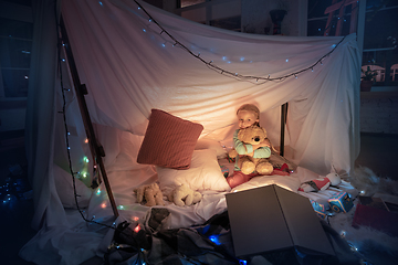 Image showing Little girl lying in a teepee, playing with the flashlight