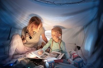 Image showing Mother and daughter sitting in a teepee, reading stories with the flashlight