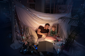 Image showing Father and daughter sitting in a teepee, having fun with the flashlight