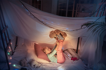 Image showing Little girl lying in a teepee, playing with the flashlight