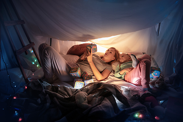 Image showing Mother and daughter sitting in a teepee, having fun with the flashlight