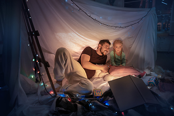 Image showing Father and daughter sitting in a teepee, having fun with the flashlight