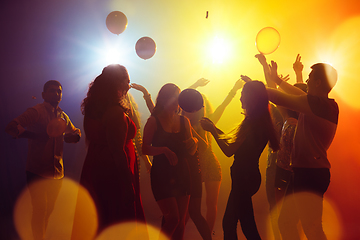 Image showing A crowd of people in silhouette raises their hands against colorful neon light on party background