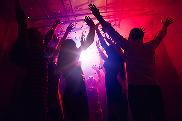 Image showing A crowd of people in silhouette raises their hands against colorful neon light on party background