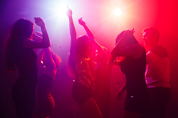 Image showing A crowd of people in silhouette raises their hands against colorful neon light on party background