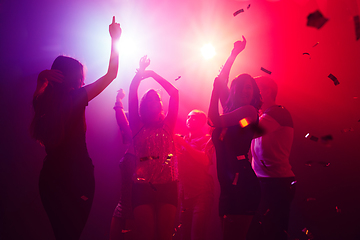 Image showing A crowd of people in silhouette raises their hands against colorful neon light on party background