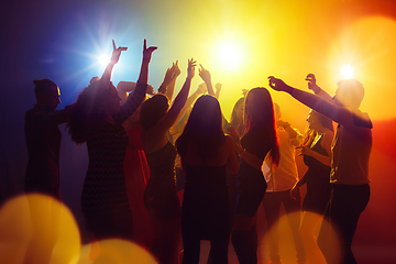 Image showing A crowd of people in silhouette raises their hands against colorful neon light on party background