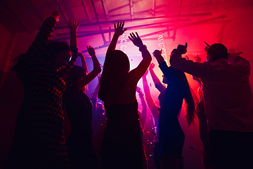 Image showing A crowd of people in silhouette raises their hands against colorful neon light on party background