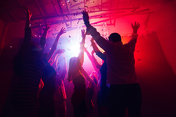 Image showing A crowd of people in silhouette raises their hands against colorful neon light on party background