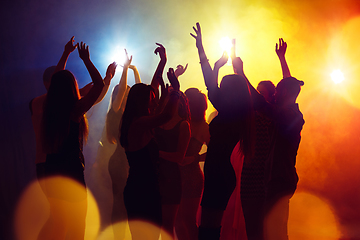 Image showing A crowd of people in silhouette raises their hands against colorful neon light on party background