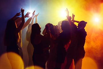 Image showing A crowd of people in silhouette raises their hands against colorful neon light on party background