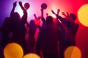 Image showing A crowd of people in silhouette raises their hands against colorful neon light on party background