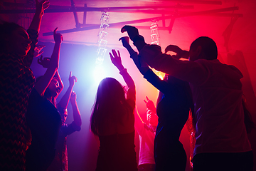 Image showing A crowd of people in silhouette raises their hands against colorful neon light on party background