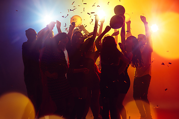 Image showing A crowd of people in silhouette raises their hands against colorful neon light on party background