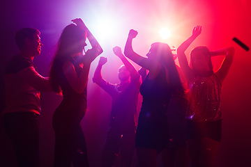 Image showing A crowd of people in silhouette raises their hands against colorful neon light on party background