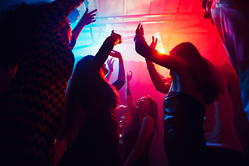 Image showing A crowd of people in silhouette raises their hands against colorful neon light on party background