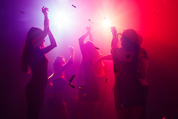 Image showing A crowd of people in silhouette raises their hands against colorful neon light on party background