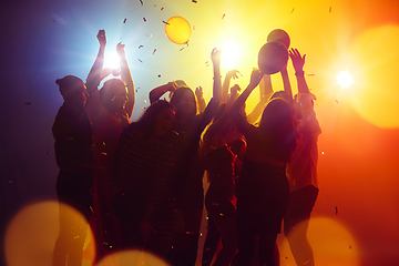 Image showing A crowd of people in silhouette raises their hands against colorful neon light on party background