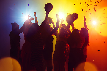 Image showing A crowd of people in silhouette raises their hands against colorful neon light on party background