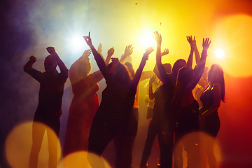 Image showing A crowd of people in silhouette raises their hands against colorful neon light on party background