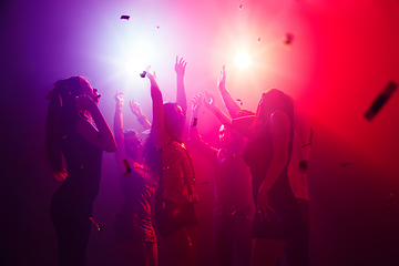 Image showing A crowd of people in silhouette raises their hands against colorful neon light on party background