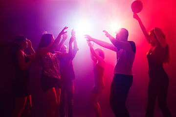 Image showing A crowd of people in silhouette raises their hands against colorful neon light on party background