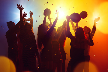 Image showing A crowd of people in silhouette raises their hands against colorful neon light on party background