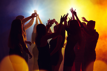 Image showing A crowd of people in silhouette raises their hands against colorful neon light on party background