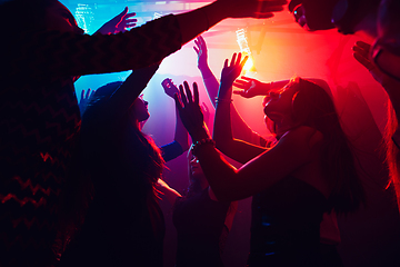 Image showing A crowd of people in silhouette raises their hands against colorful neon light on party background