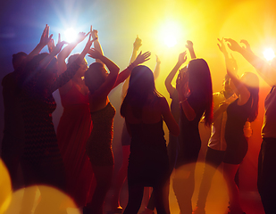 Image showing A crowd of people in silhouette raises their hands against colorful neon light on party background